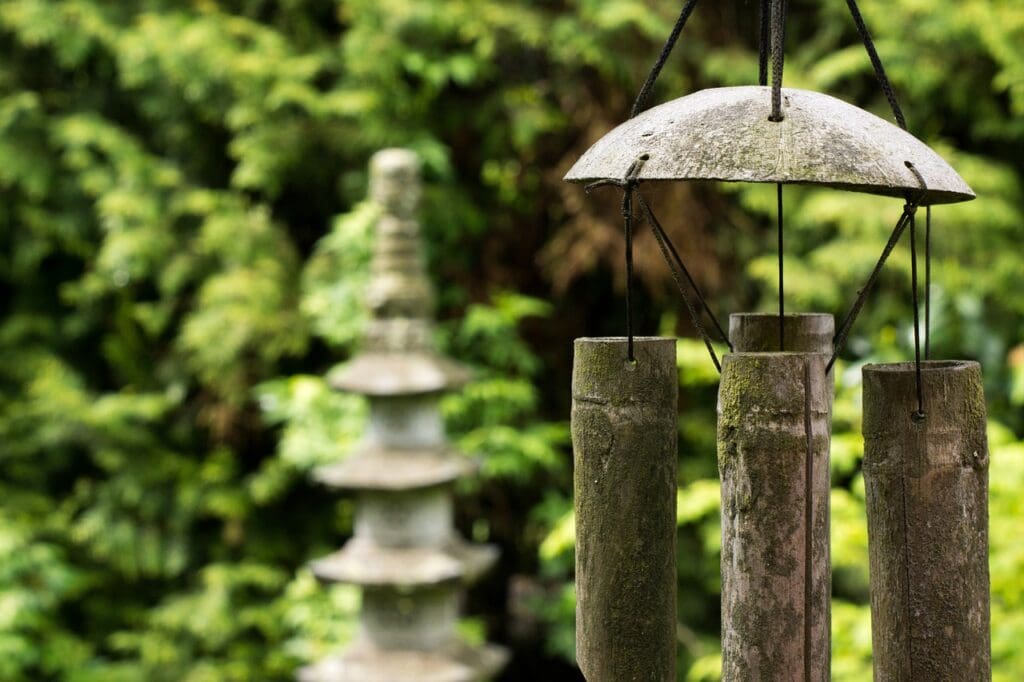 Bamboo wind chimes haning in garden with stone garden ornament in background defocused