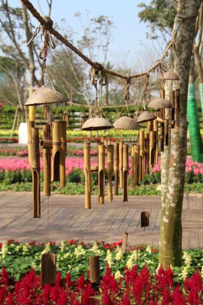 Multiple bamboo windchimes strung between two trees with garden in background
